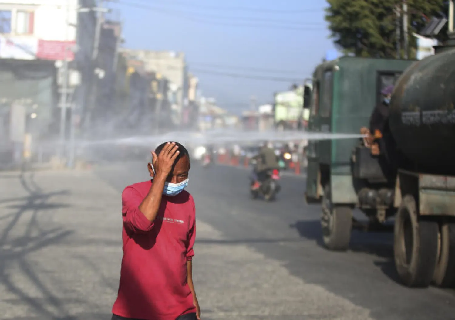 رجل يرتدي كمامة للحماية من فيروس «كورونا» يمشي مقابل شاحنة تقوم برش مواد معقمة في شوارع نيبال (أ.ب)
