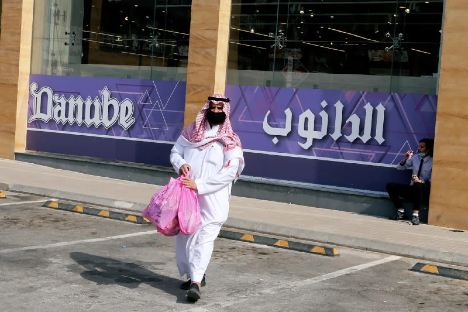 رجل سعودي يرتدي قناعاً واقياً ويسير أمام سوبر ماركت في شارع التخصصي بالرياض (رويترز)