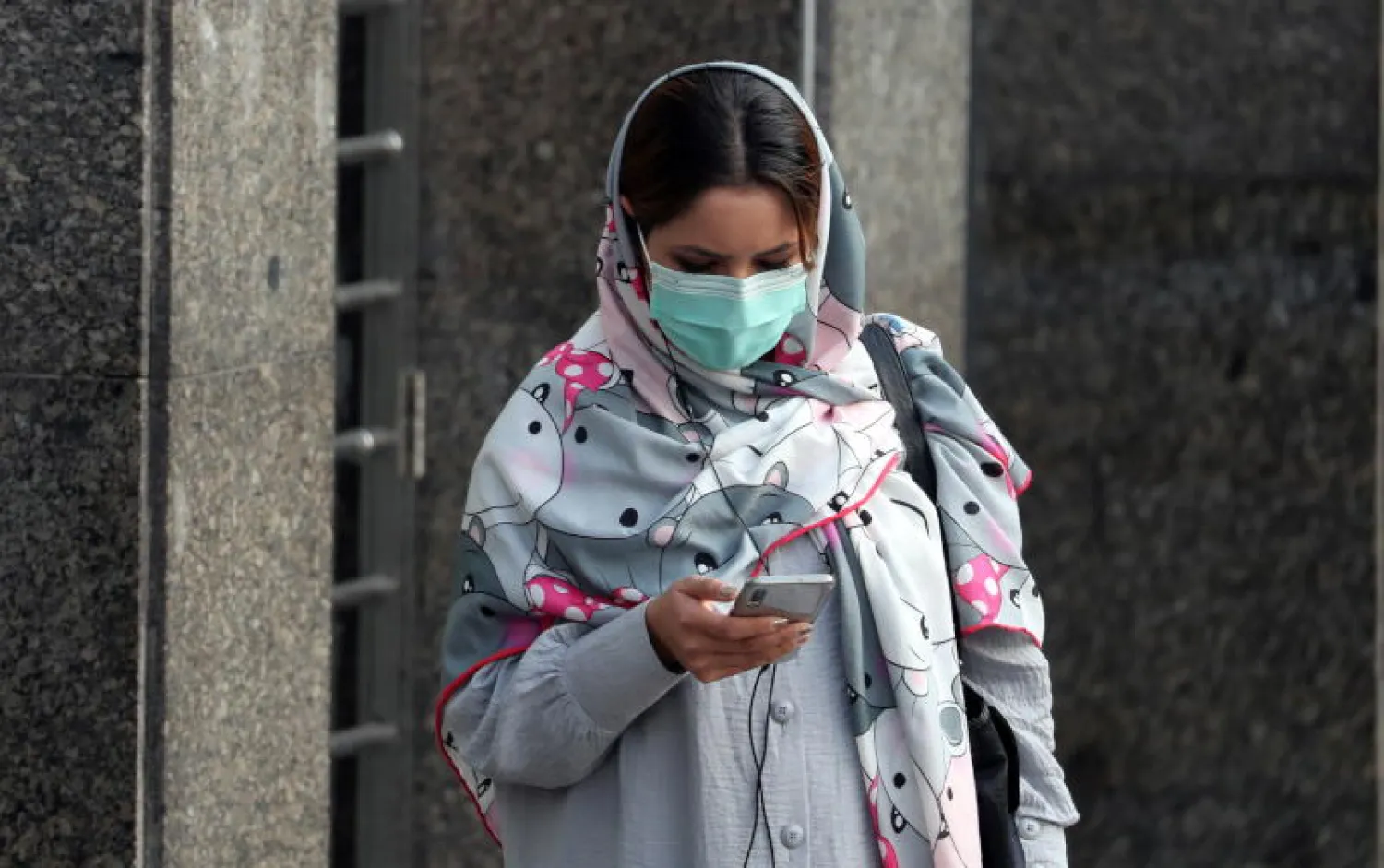 سيدة إيرانية ترتدي قناعاً واقياً وتمشي في أحد شوارع طهران (إ.ب.أ)