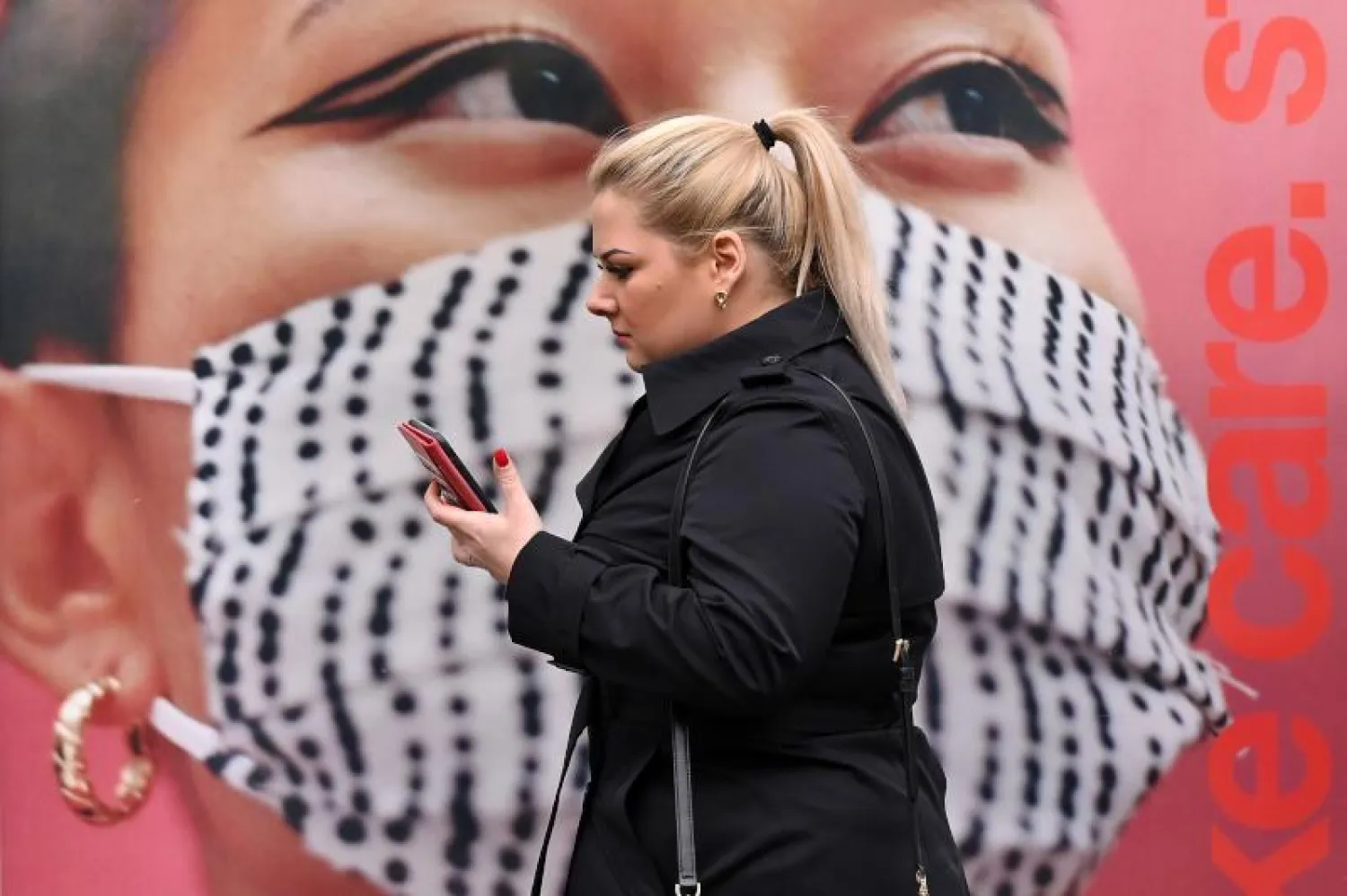 امرأة تمر في أحد شوارع لندن أمام ملصق يدعو الناس إلى وضع الكمامات (أ.ف.ب)