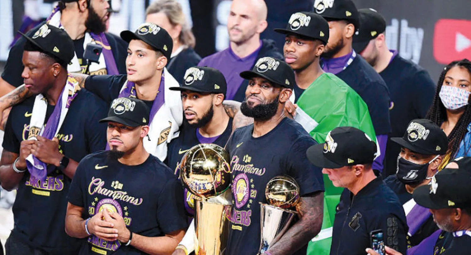 ليبرون جيمس يتوسط لاعبي الليكرز حاملاً كأسي البطولة وأفضل لاعب (أ.ف.ب)