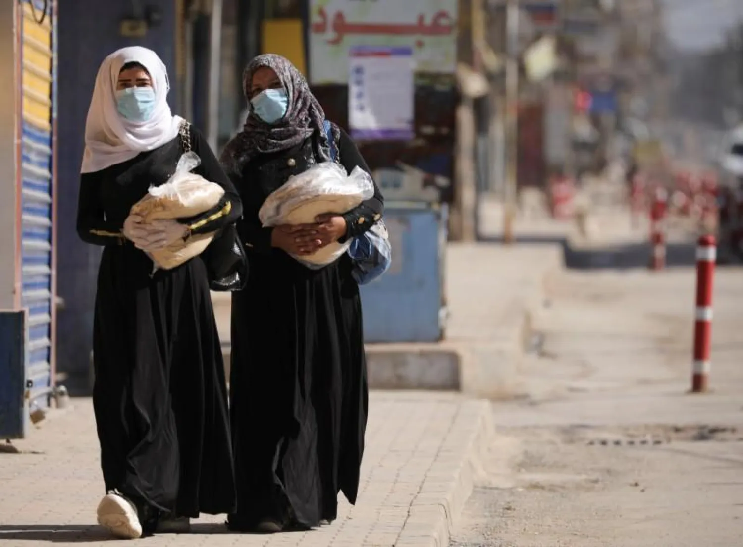 Women hold stacks of bread as they walk along an empty street, as restrictions are imposed as measure to prevent the spread of the coronavirus disease (COVID-19) in Qamishli, Syria March 23, 2020. REUTERS/Rodi Said
