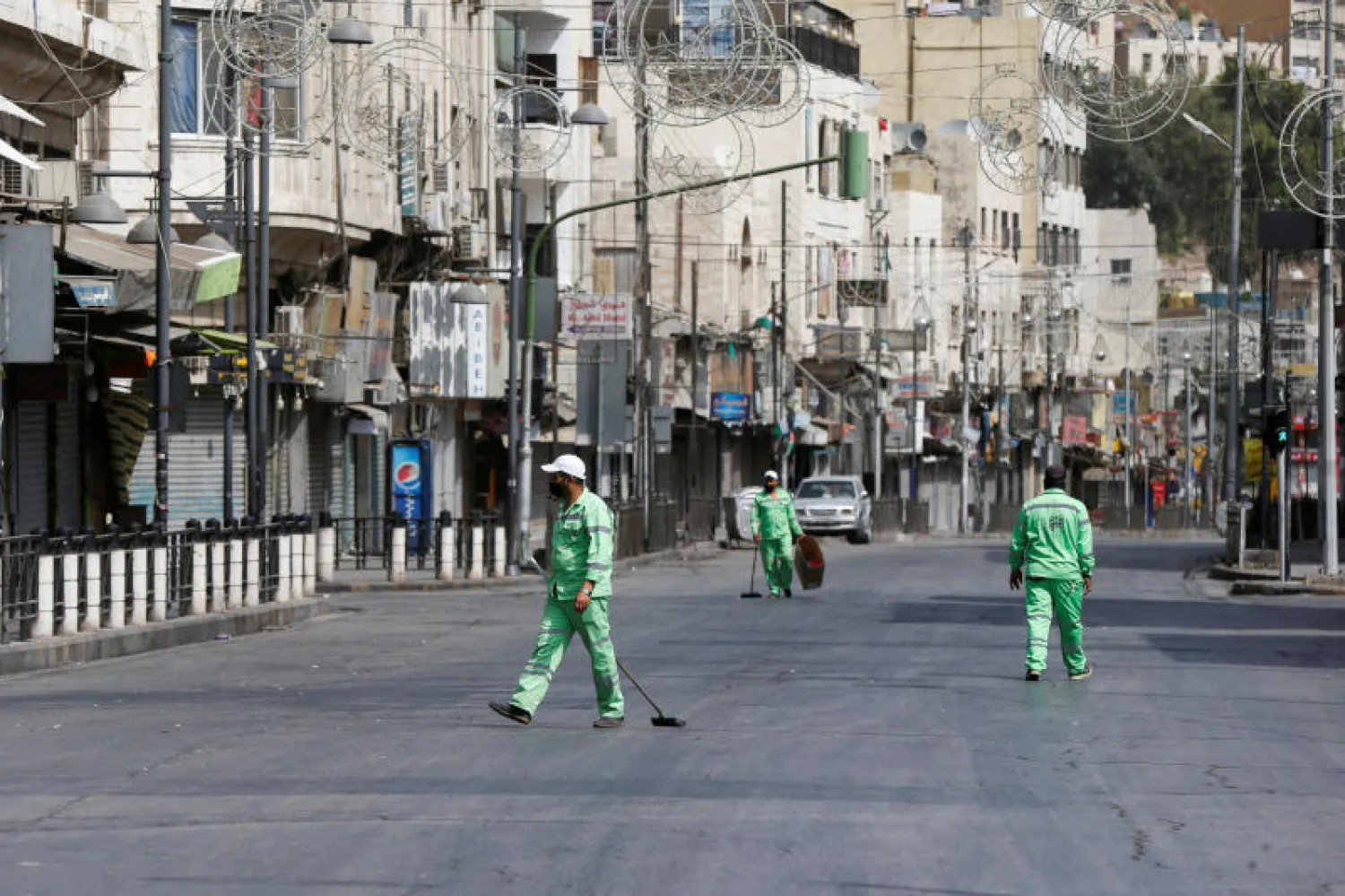 عمال نظافة يعملون خلال حظر التجول المفروض على مستوى البلاد وسط مدينة عمّان (رويترز)