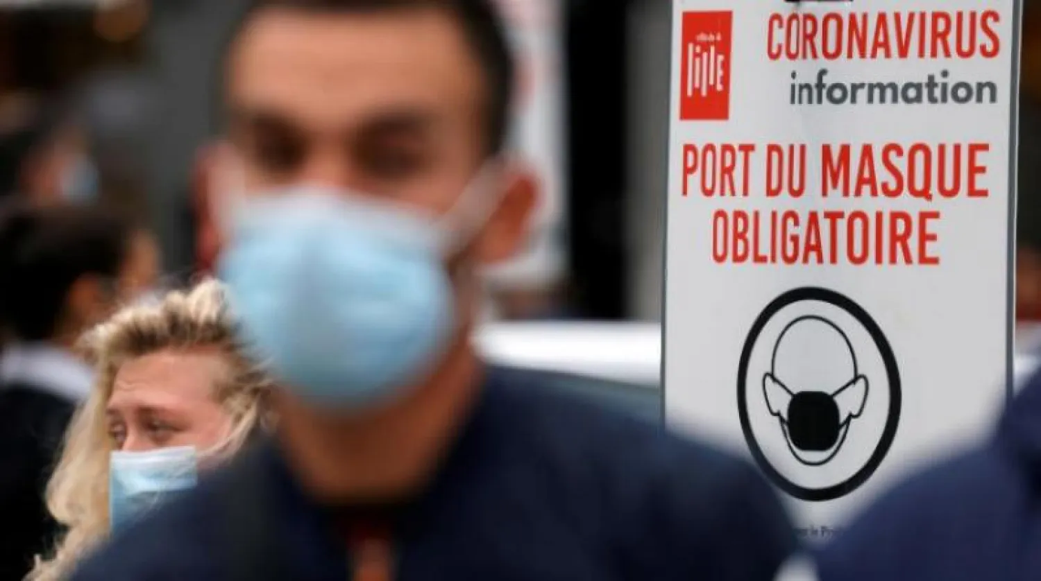 أشخاص يمشون أمام لافتة كتب عليها «إلزامي ارتداء قناع» في شوارع باريس (رويترز)