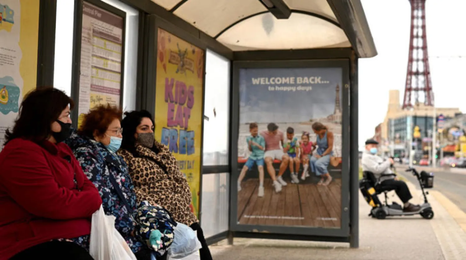 نسوة بكمامات للوقاية من «كورونا» عند موقف للحافلات في مدينة بلاكبول الإنجليزية أمس (أ.ف.ب)