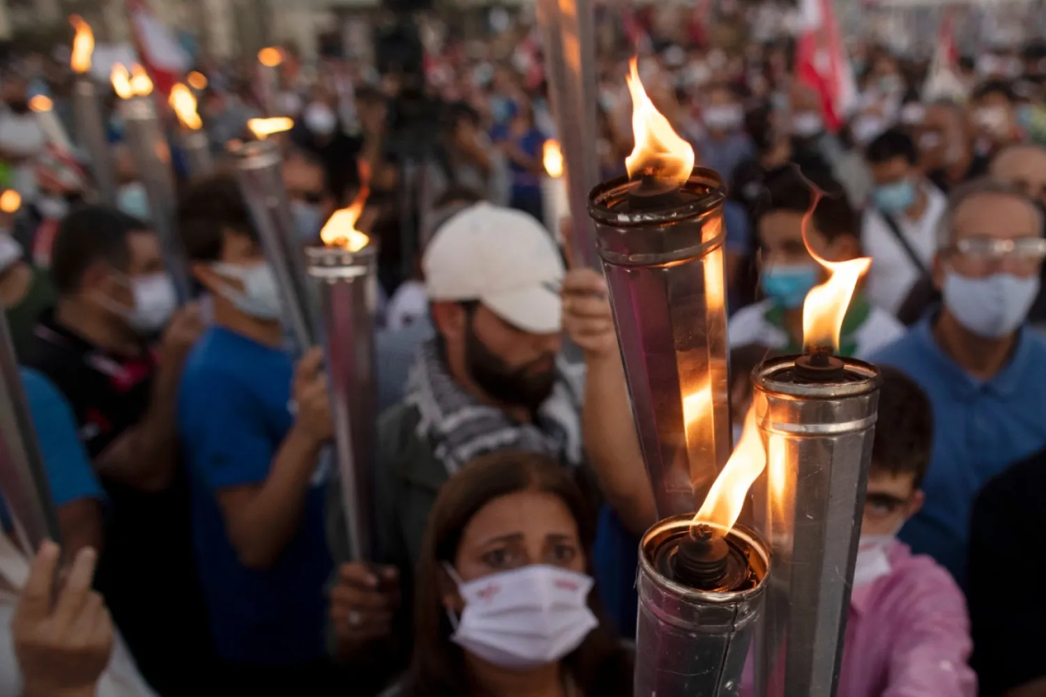 Anti-government protesters hold up torches as they lit a giant flame over a metal statue that reads in Arabic: "October 17, Revolution." next to the site of the Aug. 4 deadly blast in the seaport of Beirut that killed scores and wounded thousands in Beirut, Lebanon, Saturday, Oct. 17, 2020. (AP Photo/Hassan Ammar)