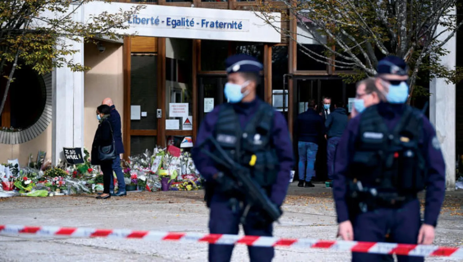 شرطيان وأكاليل من الورود خارج مدرسة كونفلان سانت هونورين (شمال باريس) أمس تكريماً لمدرس التاريخ المقتول (أ.ف.ب)