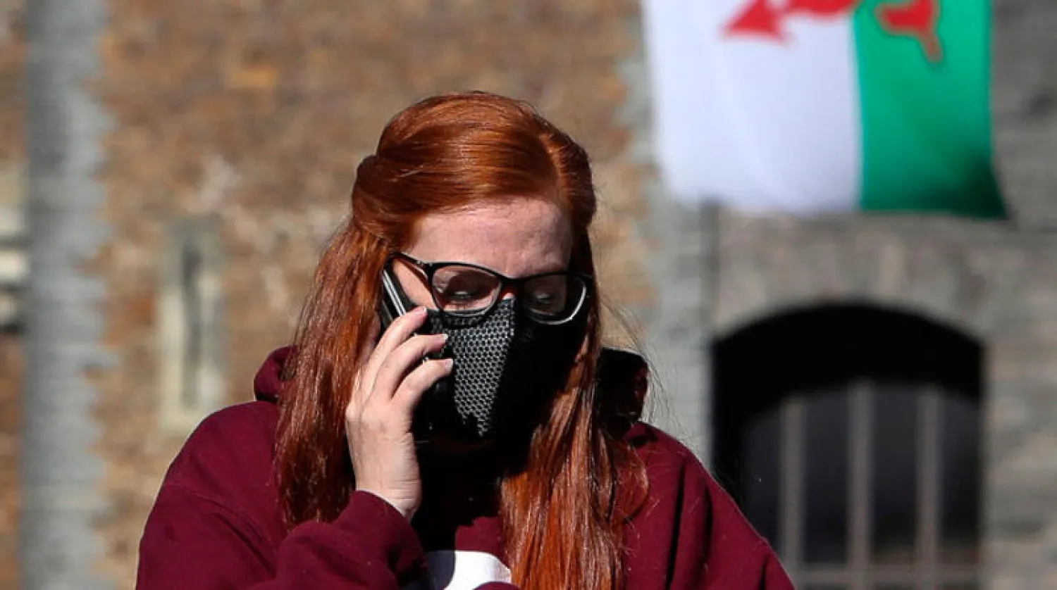 امرأة تضع قناع وجه وتتحدث في هاتفها في كارديف بإقليم ويلز (أ.ف.ب)