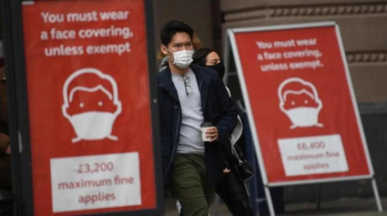 Londra’da Kovid-19 salgını ile mücadele kapsamında alınan yeni önlemleri gösteren iki tabela arasından geçen maskeli bir adam (EPA)