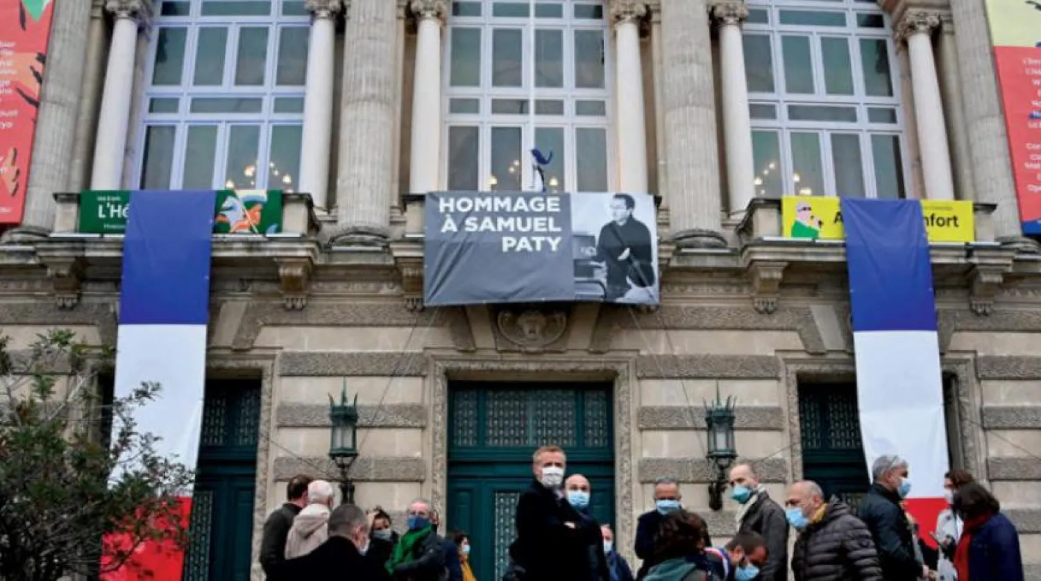 People stand in front of a portrait of French teacher Samuel Paty displayed on the facade of the Opera Comedie in Montpellier on October 21, 2020, during a national homage to the teacher who was beheaded. (Photo by Pascal GUYOT / AFP)