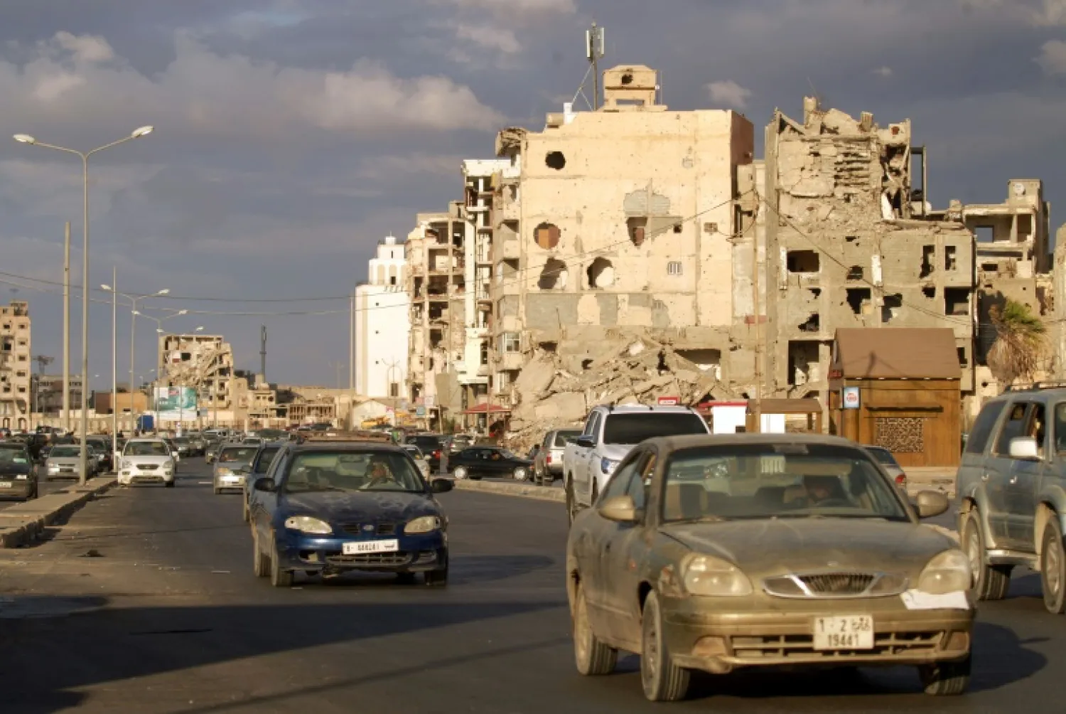 Motorists drive past war-damaged buildings in Libya's main eastern city of Benghazi, where businessmen are desperate for Friday's "permanent" ceasefire to reopen trade with the unity government-held west | AFP