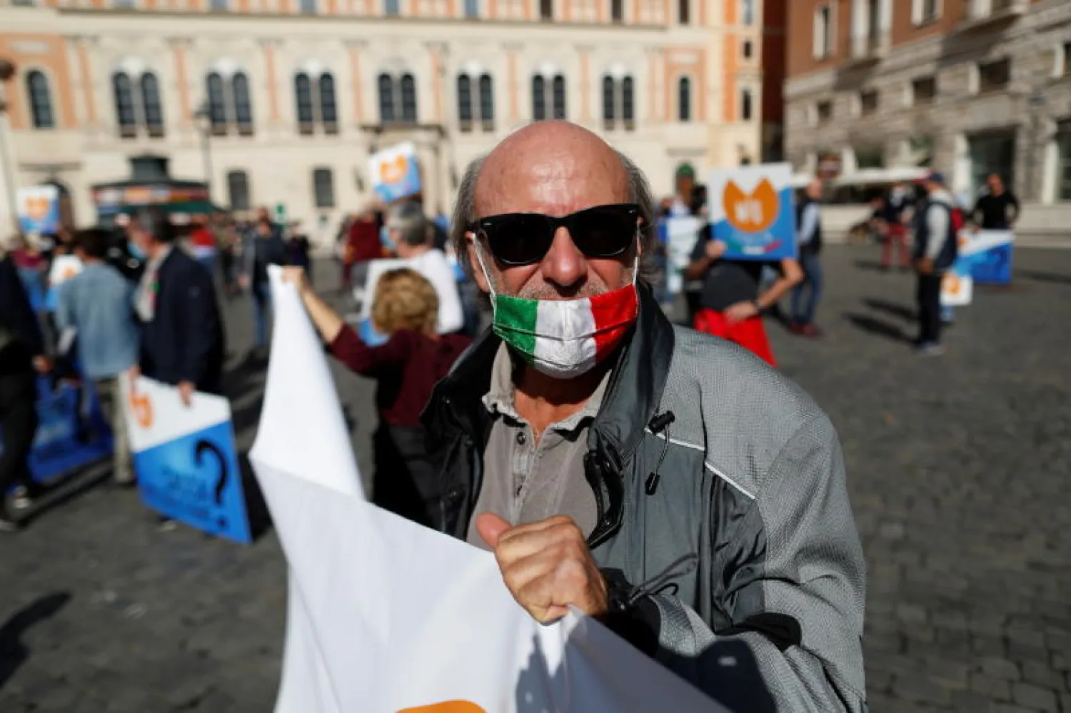 متظاهر يرتدي قناعاً يحمل علم إيطاليا خلال احتجاجات مناهضة للقيود المشددة التي تفرضها الحكومة لمكافحة تفشي فيروس كورونا في روما (رويترز)