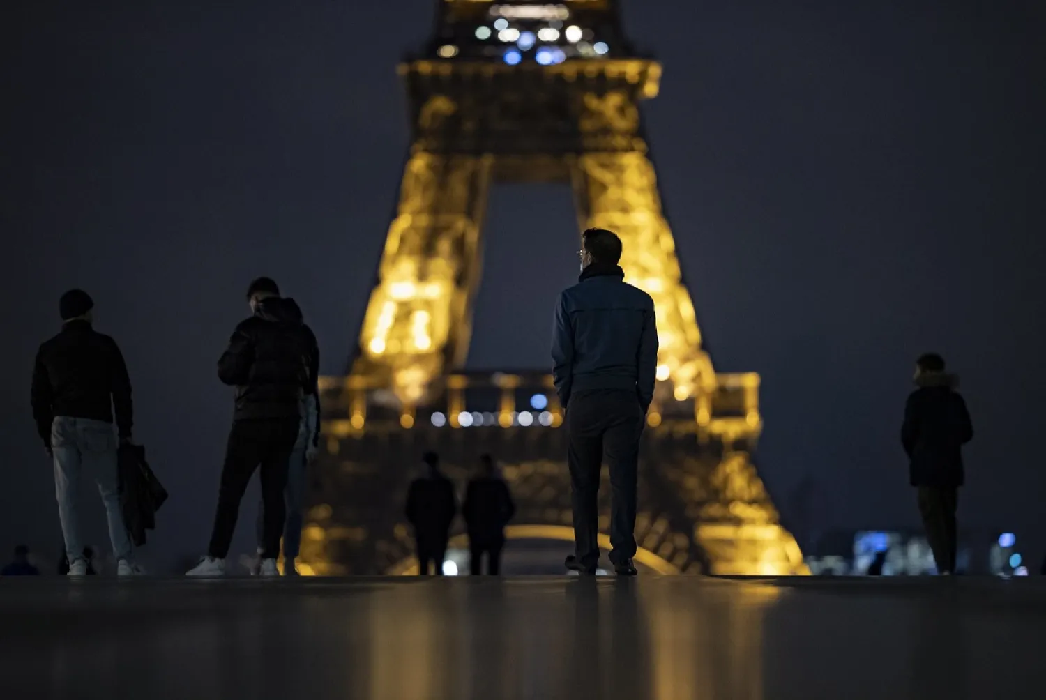 People wearing protective face masks walk near the Eiffel Tower at nightfall, just hours before a city-wide night-time curfew goes into effect in Paris, France, Oct. 16, 2020. (EPA)