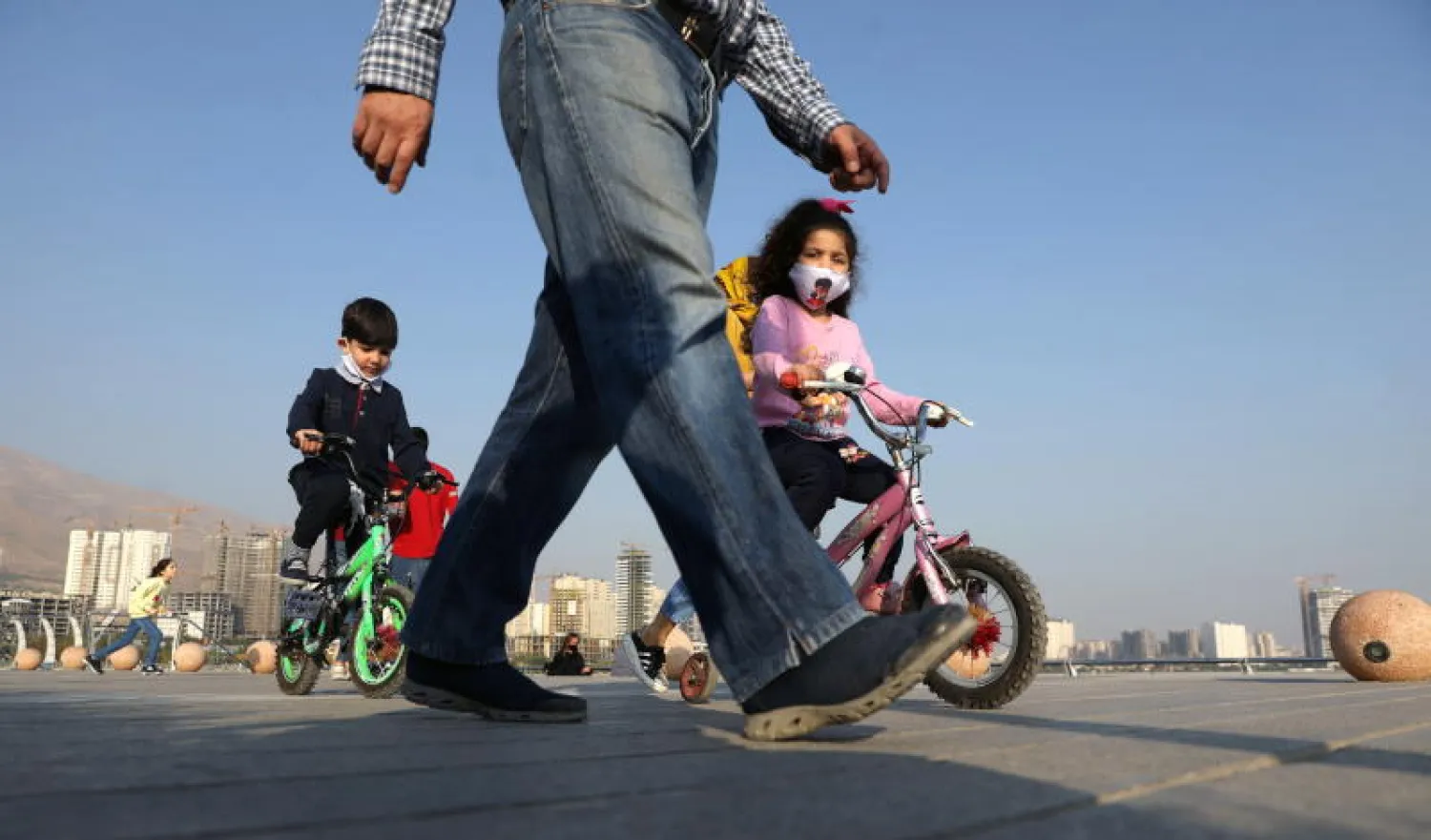 أطفال إيرانيون على دراجاتهم يرتدون الأقنعة الواقية وسط تفشي فيروس كورونا في البلاد (رويترز)