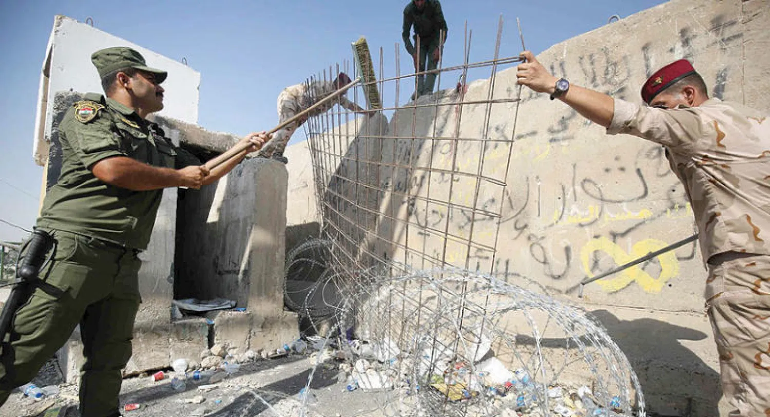 عناصر أمن يزيلون أسلاكاً شائكة وحاجزاً كونكريتياً من على جسر السنك وسط بغداد أمس (أ.ف.ب)