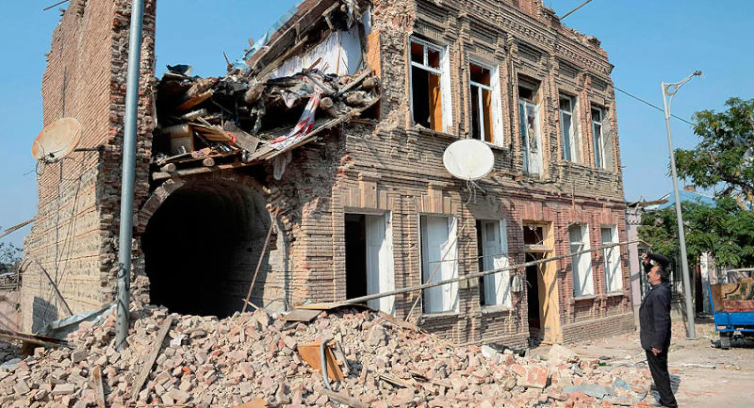 مواطن يتفقد أمس أضراراً لحقت بمبنى مدني في مدينة غنجة الأذربيجانية جراء المعارك الدائرة في قره باغ (أ.ف.ب)