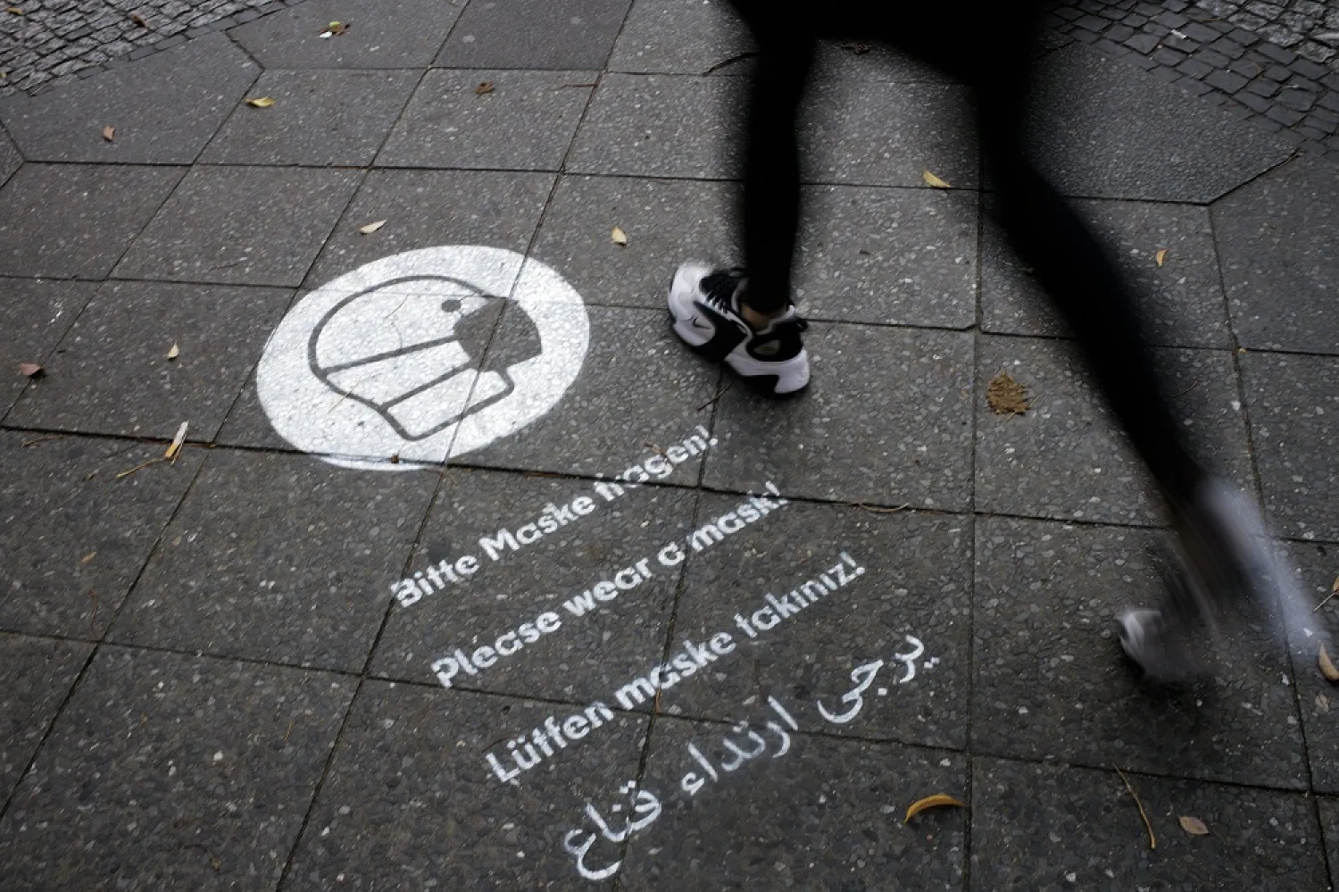A pedestrian walks over a reminder to wear face masks sprayed on the sidewalk at the Karl-Marx-Strasse at the district Neukoelln in Berlin, Germany, Oct. 27, 2020. (AP)