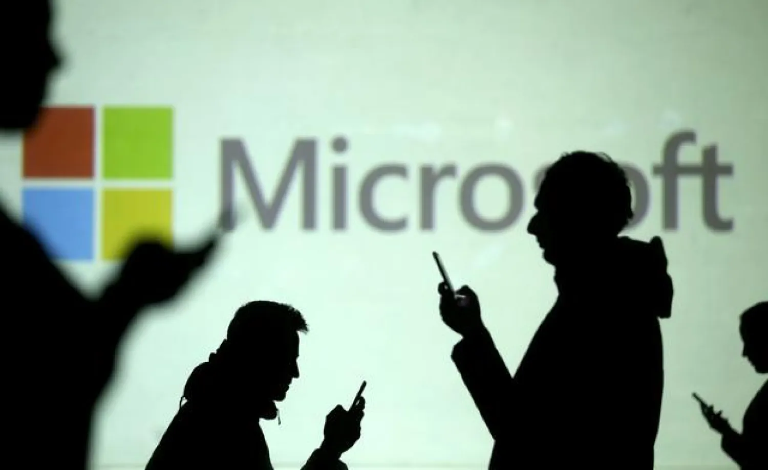 FILE PHOTO: Silhouettes of mobile users are seen next to a screen projection of Microsoft logo in this picture illustration taken March 28, 2018. REUTERS/Dado Ruvic/Illustration