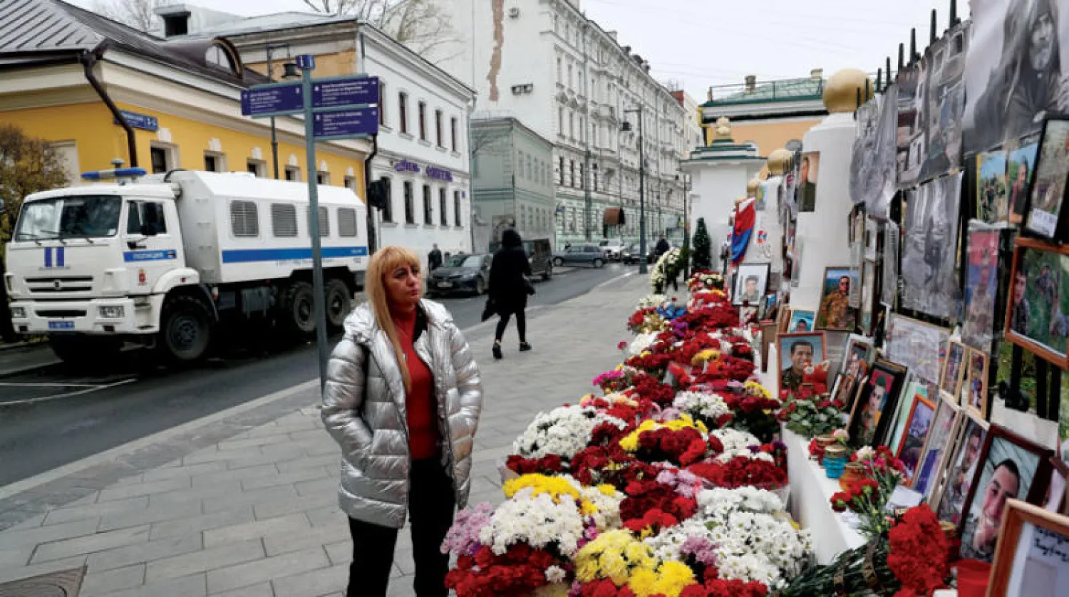 امرأة أمام باقات ورود وصور لضحايا القتال في قره باغ أمام سفارة أرمينيا في موسكو أمس (رويترز)