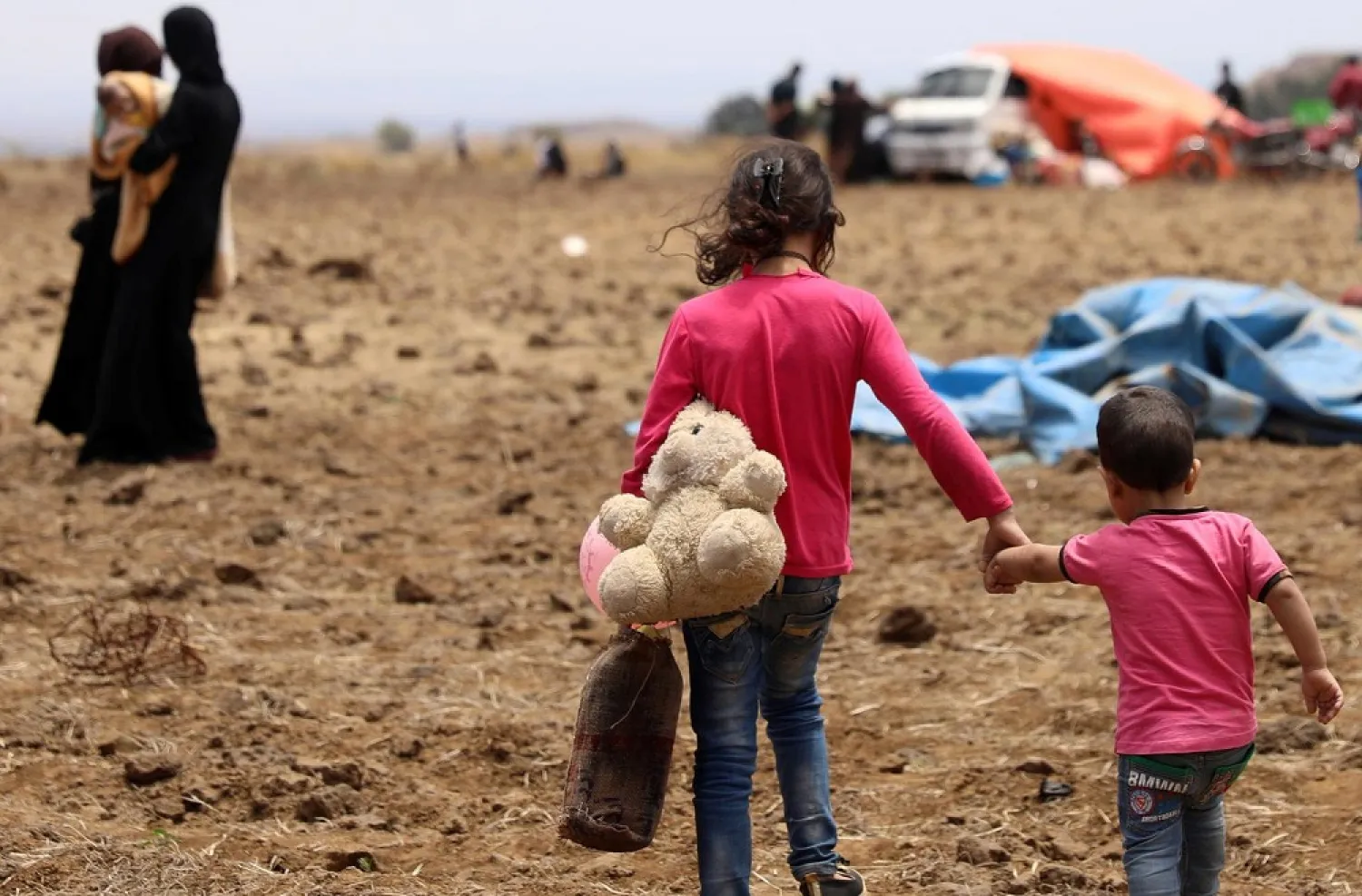 An internally displaced girl from Daraa province carries a stuffed toy and holds the hand of child near the Israeli-occupied Golan Heights in Quneitra, Syria June 29, 2018. (Reuters)