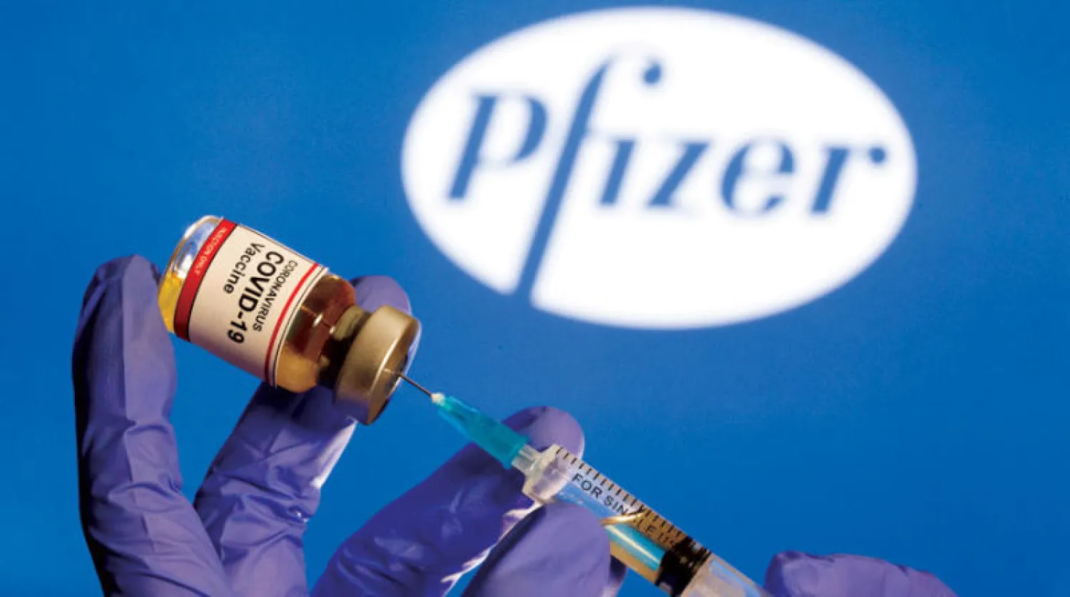 امرأة تحمل علبة صغيرة عليها علامة لقاح «كوفيد - 19» أمام شعار لشركة «فايزر» نهاية الشهر الماضي (رويترز)