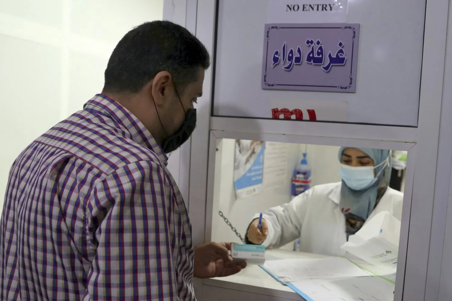 Hassan Taha, who suffers from a heart condition, receives medication from a pharmacist at the Amel Association, a Lebanese humanitarian group, in Dahiyeh, a southern suburb of Beirut, Lebanon, Tuesday, Nov. 3, 2020. Lebanese have been forced to search far and wide for their prescriptions after many medications vanished from pharmacies. It's the latest chapter in their country's financial breakdown. (AP Photo/Bilal Hussein)
