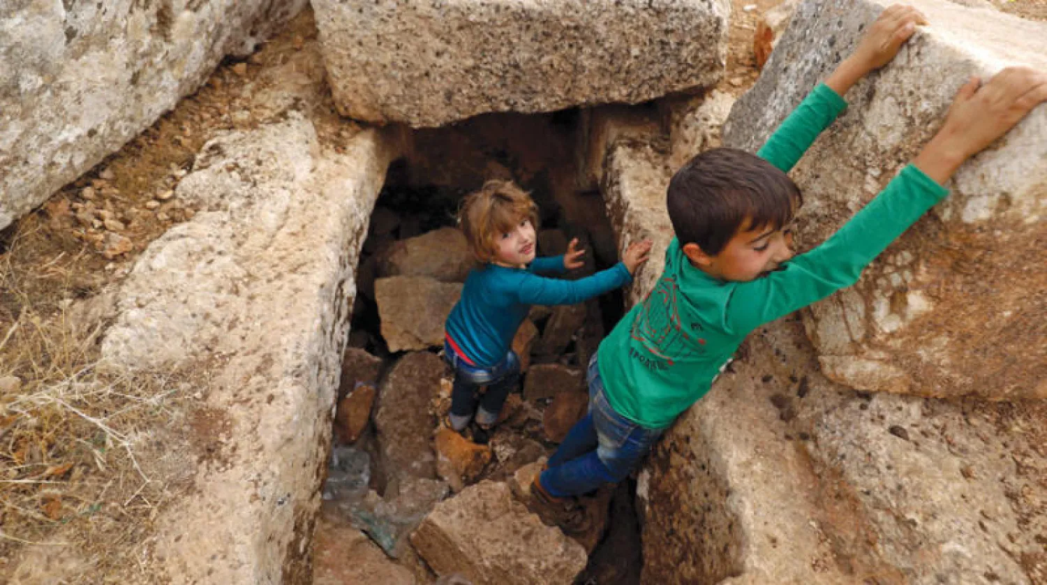 طفلان نازحان يلعبان على بقايا آثار رومانية شمال غربي سوريا (أ.ف.ب)