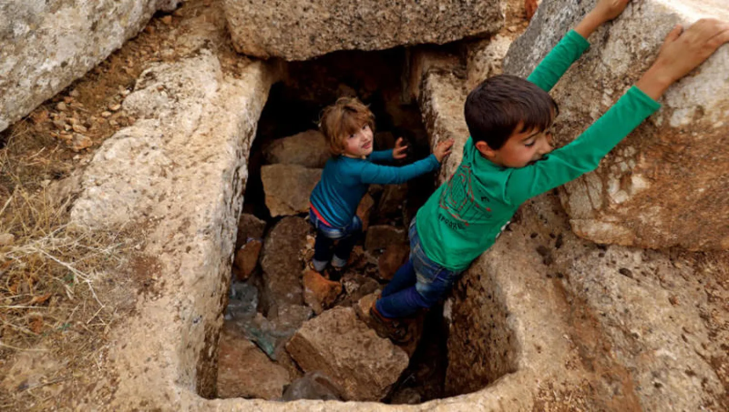 طفلان نازحان يلعبان على بقايا آثار رومانية شمال غربي سوريا (أ.ف.ب)