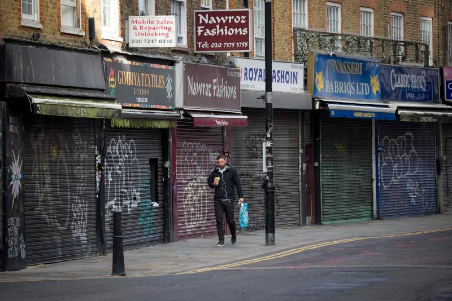 رجل يسير أمام محال مغلقة بفعل الجائحة في لندن (أ.ف.ب)