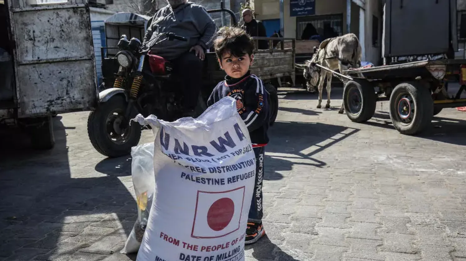 A child next to a sack of flour as people come to receive food aid from the UN's agency for Palestinian refugees in the Khan Yunis camp in the southern Gaza Strip | AFP