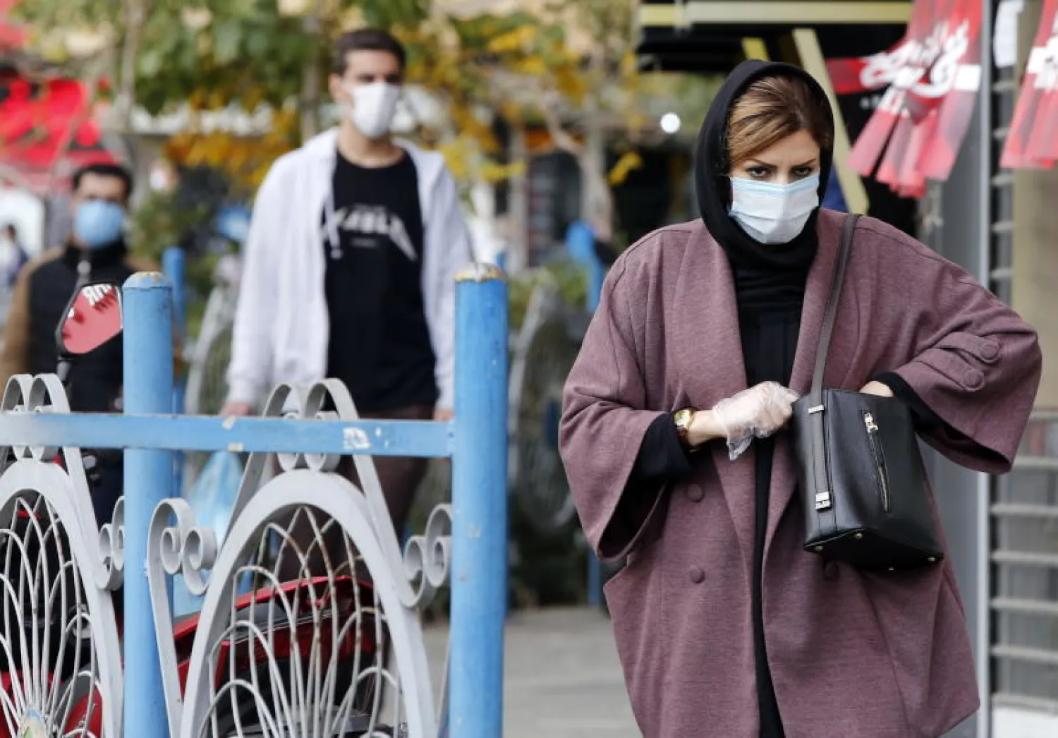 سيدة إيرانية ترتدي قناعاً واقياً وتمشي في شارع بالعاصمة طهران (رويترز)