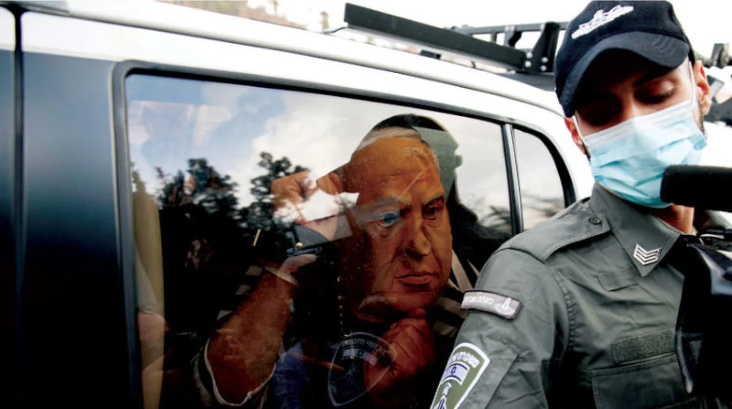 متظاهر يرتدي قناعاً يمثل وجه نتنياهو داخل سيارة شرطة بتهمة إغلاق الطريق إلى القدس (رويترز)