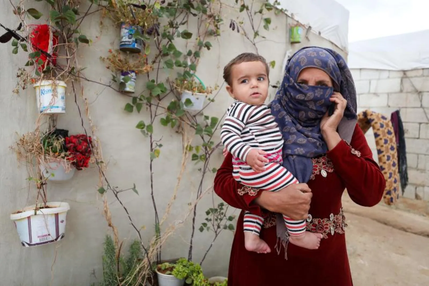 سيدة سورية في إدلب تحمل طفلها وتصنع من حجابها قناعا واقيا (أرشيفية - أ.ف.ب)