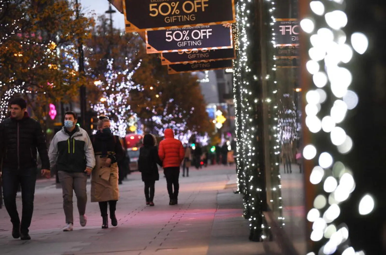 متسوقون يمرون أمام نوافذ المتاجر المزينة بهدايا عيد الميلاد بشارع أكسفورد في لندن (إ.ب.أ)