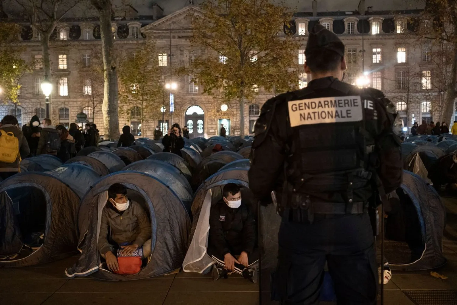 A police officer stands in front of migrants in a makeshift camp set up Monday night Nov.23, 2020 on Place de la Republique in Paris. Paris police are under government orders to explain themselves after officers were filmed tossing migrants out of tents while evacuating a makeshift camp in the French capital. (Alexandra Henry/Utopia56 via AP)