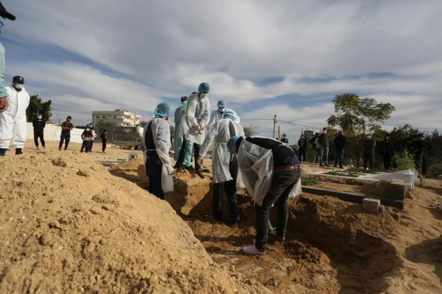 عمال يرتدون بدلات واقية يحفرون قبراً خلال جنازة امرأة توفيت بسبب فيروس كورونا في دير البلح (د.ب.أ)