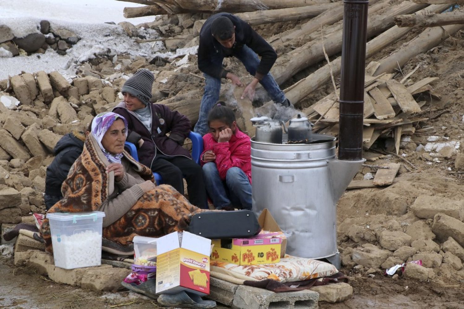 FILE: People try to warm up around a stove outside their collapsed house after an earthquake hit villages in Baskale town in Van province, Turkey, at the border with Iran, Sunday, Feb. 23, 2020. AP
