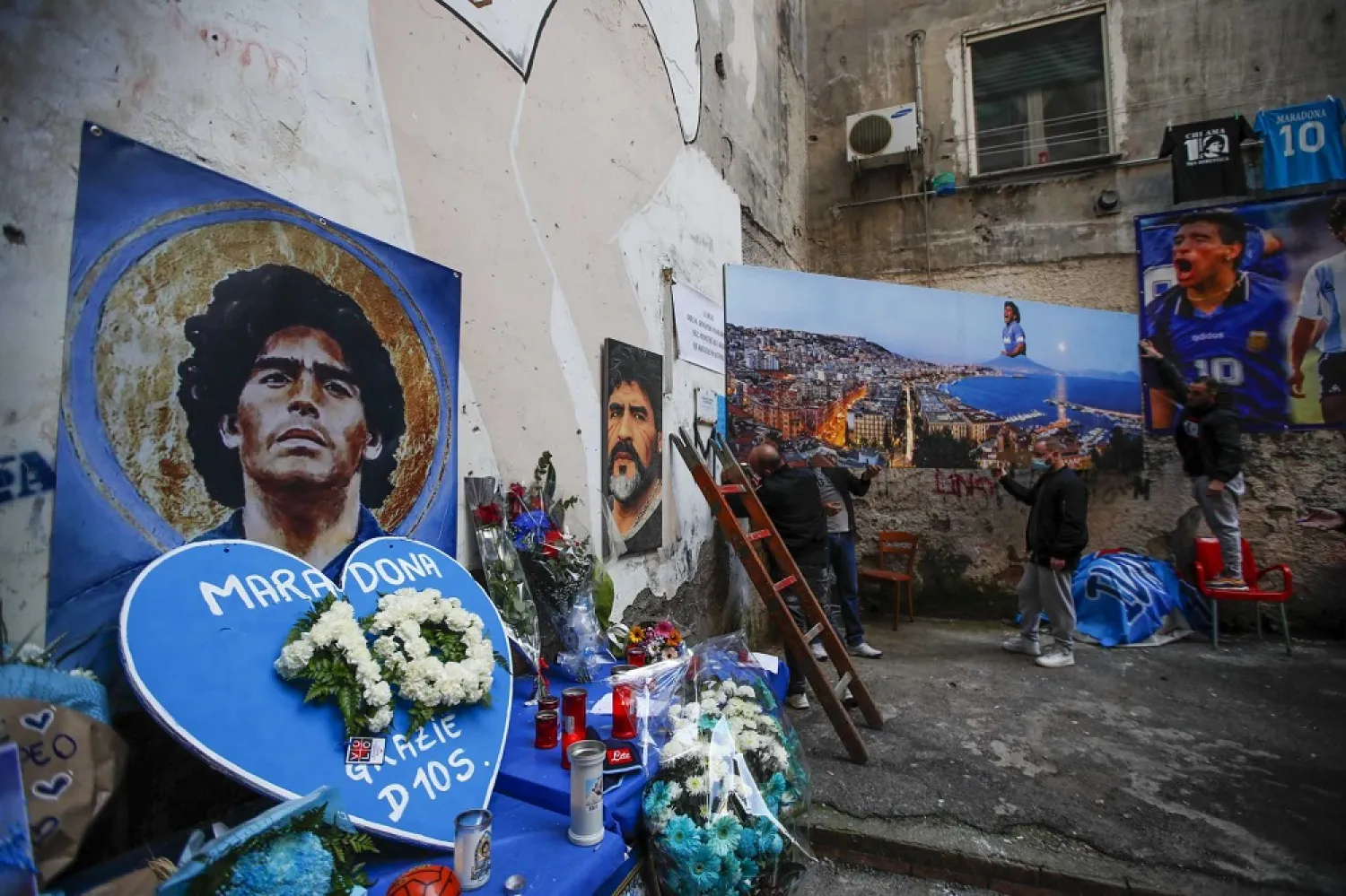 Men hang on a wall a giant photo of the Gulf of Naples with legend Diego Maradona topping the Vesuvius volcano, in Naples, Friday, Nov. 27, 2020. (AP)