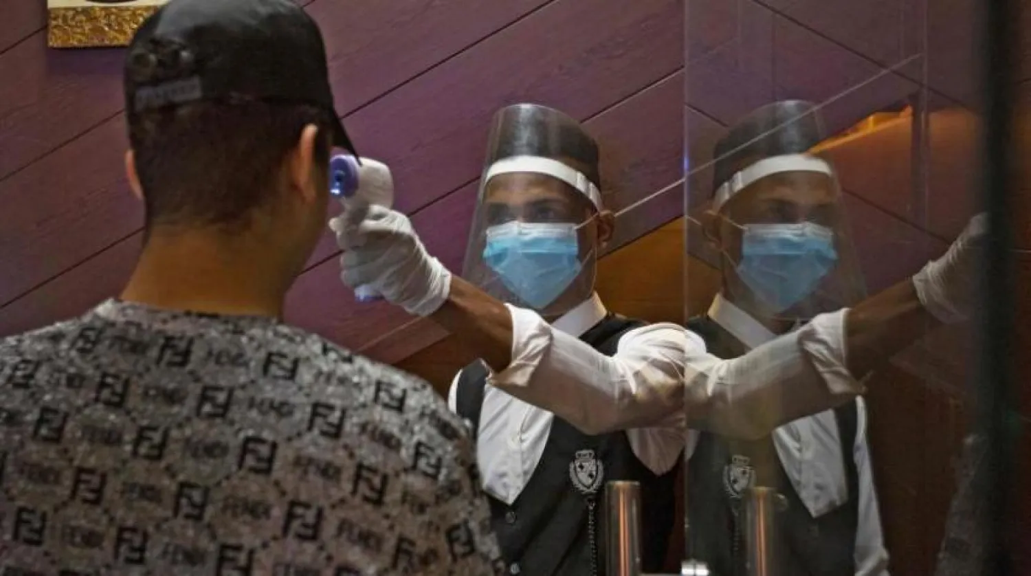 Salgından korunmak için koruyucu maske takan bir garson, Irak'taki bir restoranda bir müşterinin ateşini ölçüyor (AFP)
