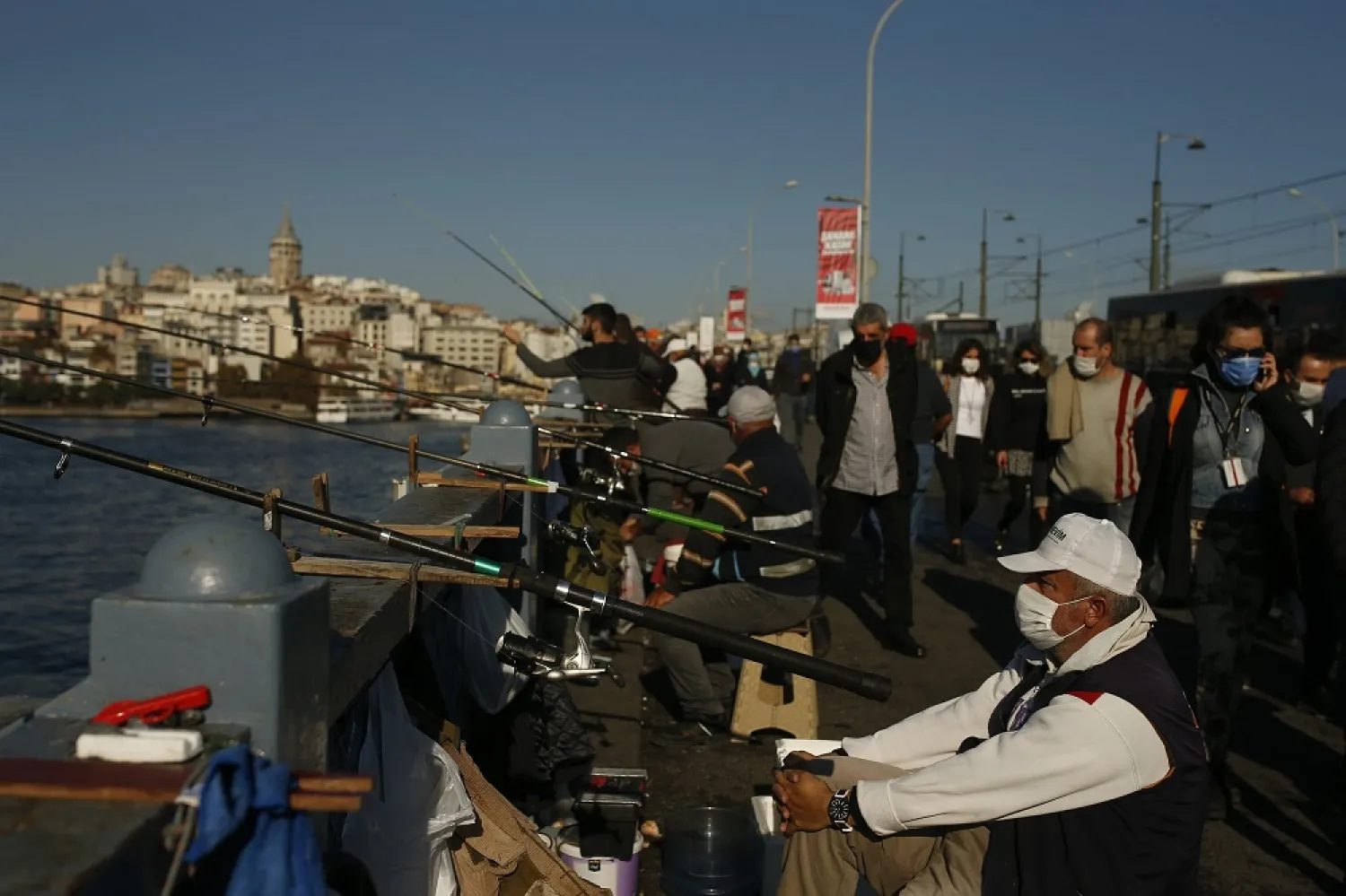 People wearing masks for protection against the coronavirus, fish from the Galata bridge over the Golden Horn in Istanbul, Tuesday, Nov. 17, 2020. (AP)