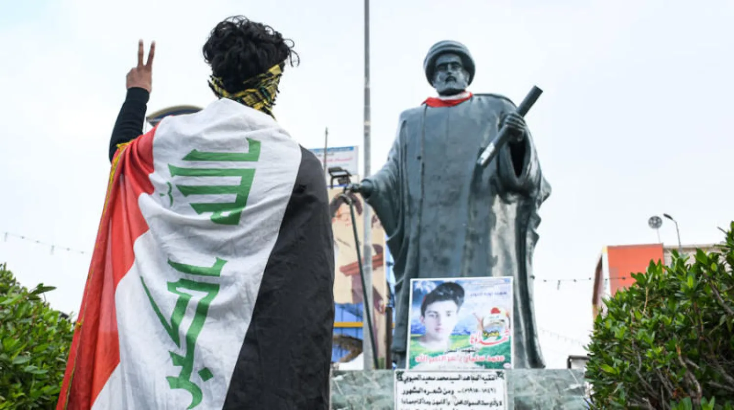 ناشط يلوح بعلامة النصر أمام تمثال للشاعر محمد سعيد الحبوبي في الناصرية أول من أمس (أ.ف.ب)