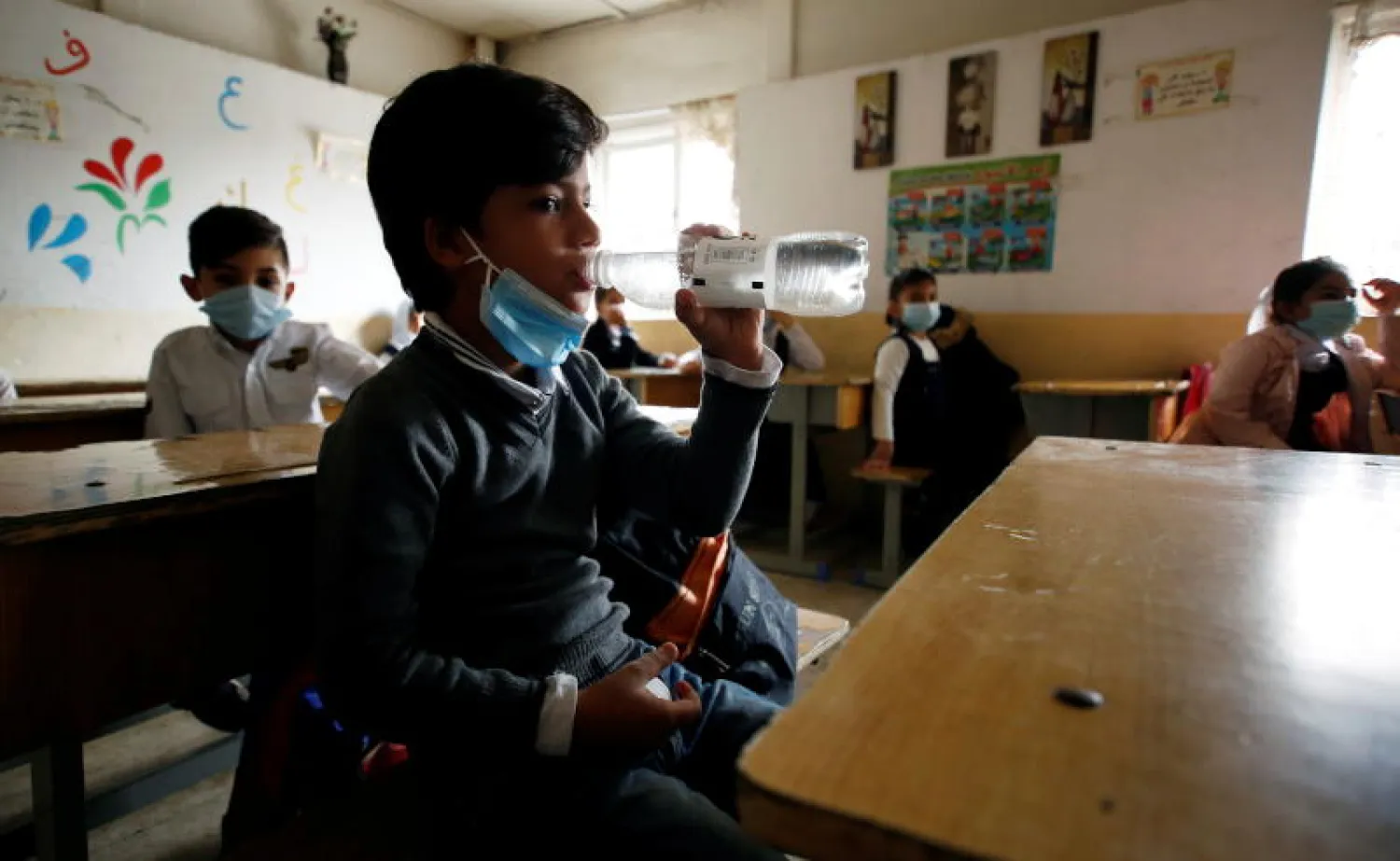 طالب عراقي يشرب الماء في فصله الدراسي بعد إعادة فتح المدارس ببغداد (رويترز)