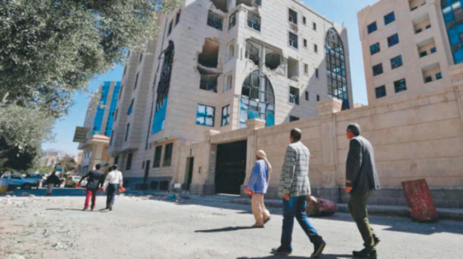 يمنيون يسيرون بالقرب من مبنى شهد اشتباكات بين أنصار صالح والحوثيين مطلع ديسمبر 2017 (أ.ف.ب)