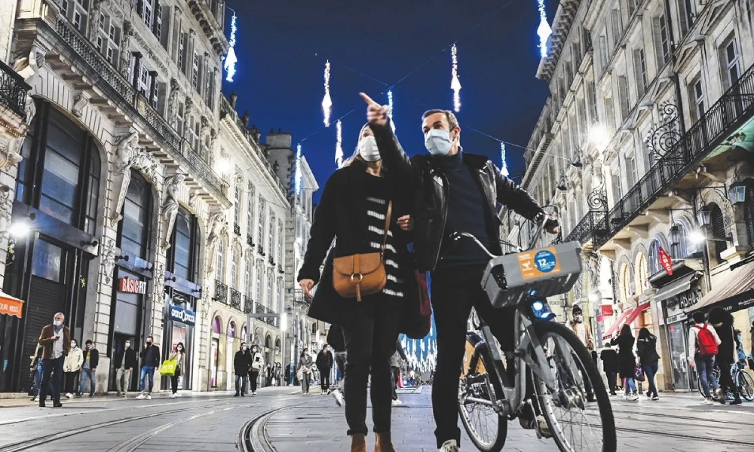 A man and a woman stand under Christmas decorations as people do shopping in Bordeaux, France. (AFP)