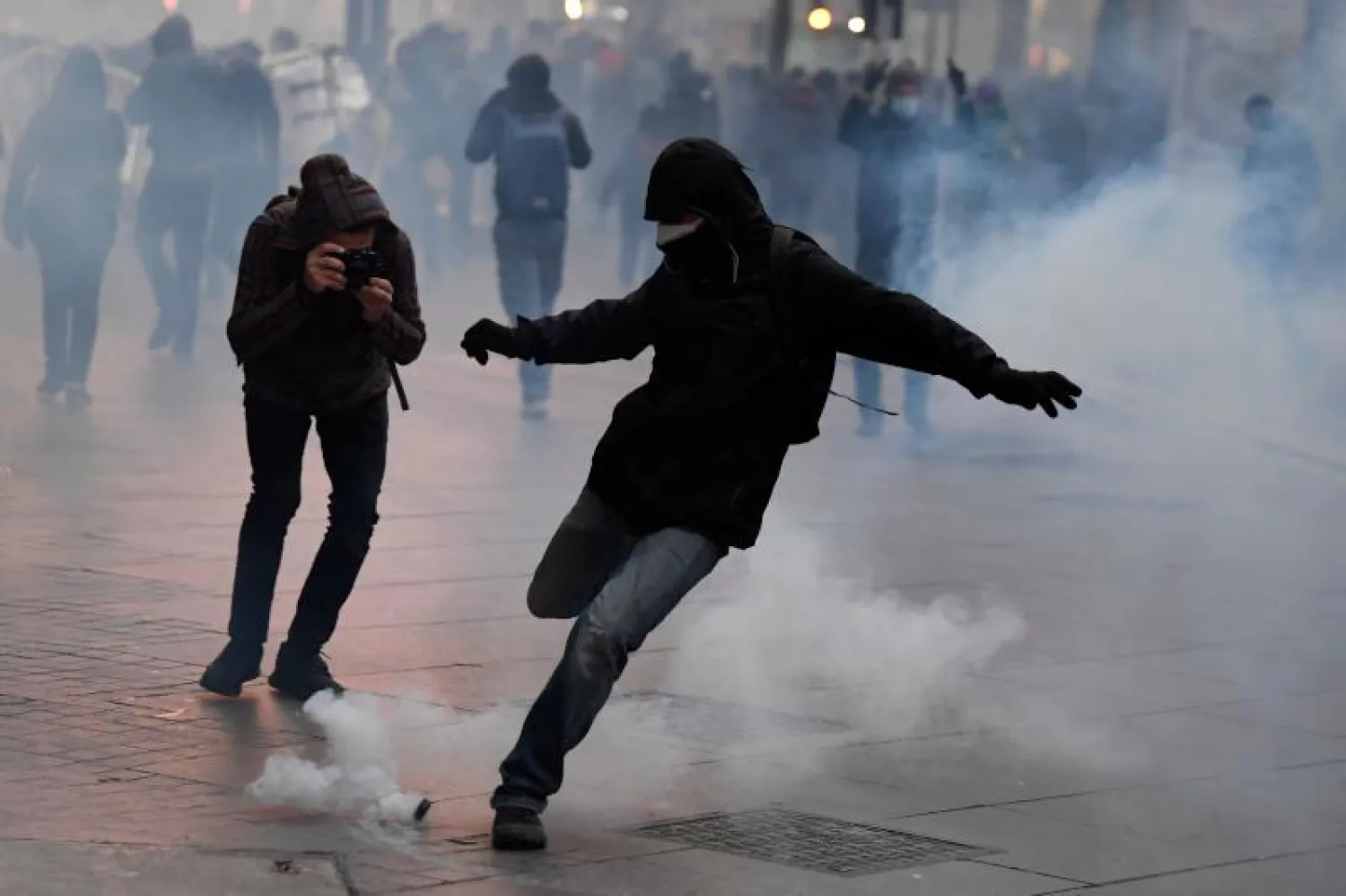 متظاهر يركل قنبلة غاز ألقتها عناصر من الشرطة الفرنسية (أ.ف.ب)