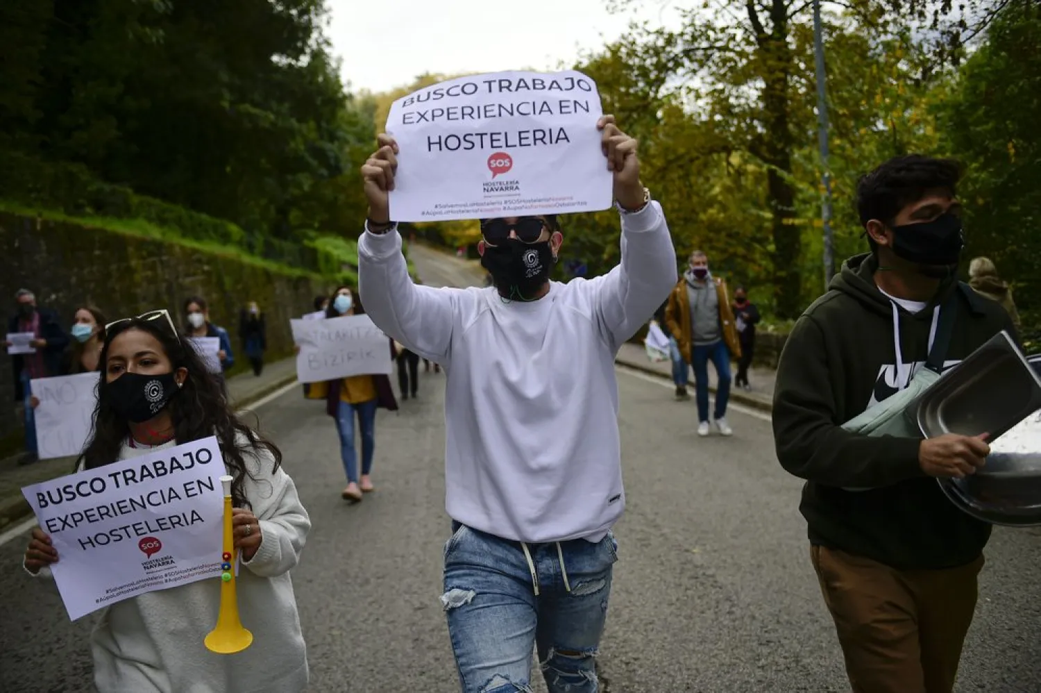 People hold up banners in support of the hotel industry that read: "I search for work", in Pamplona, northern Spain, Wednesday, Oct. 21, 2020, while protesting with others against the new measures against the coronavirus in the Navarra province where all bar and restaurants will be closed for 15 days from midnight Wednesday. (AP Photo/Alvaro Barrientos)
