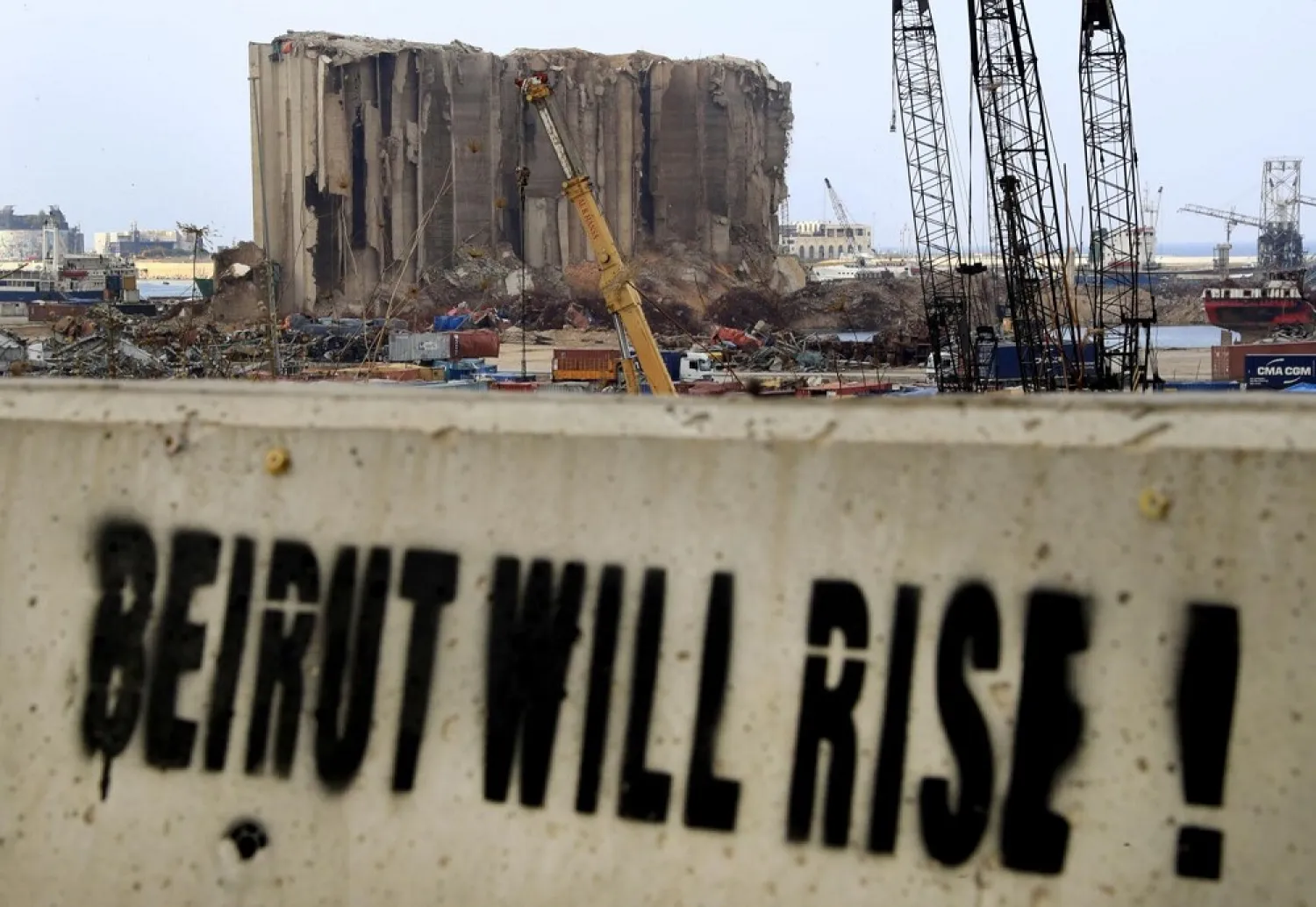 A slogan is painted on a barrier in front of towering grain silos gutted in the massive August explosion at the Beirut port, in Beirut, Lebanon, Dec. 2, 2020. (AP)