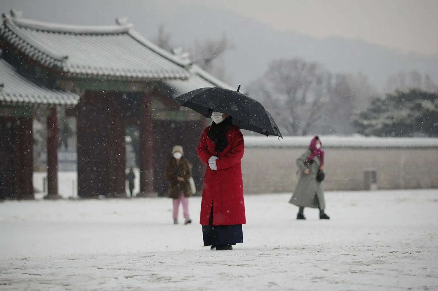 An employee wearing a face mask as a precaution against the coronavirus uses an umbrella to take shelter from the snow at the Gyeongbok Palace, in Seoul, South Korea, Dec. 13, 2020. (AP)