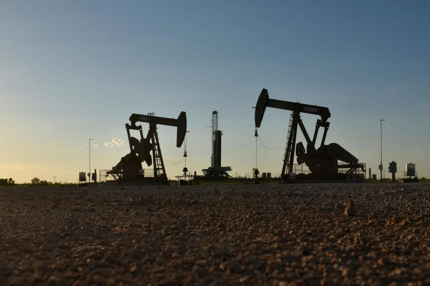 FILE PHOTO: Pump jacks operate in front of a drilling rig in an oil field in Midland, Texas US August 22, 2018. REUTERS/Nick Oxford/File Photo