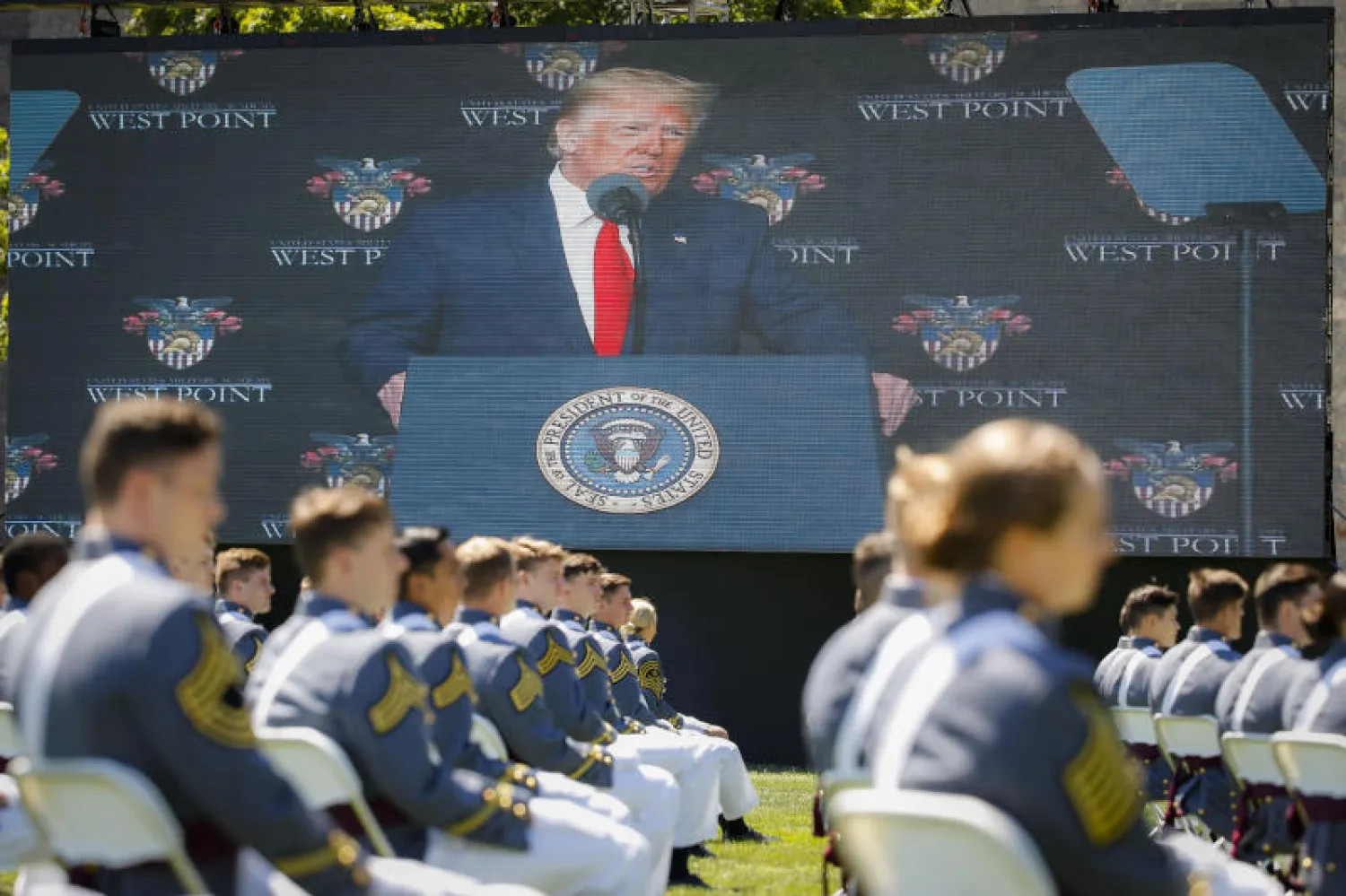 طلاب من الأكاديمية العسكرية الأميركية خلال حفل للتخرد وخلفهم صورة للرئيس دونالد ترمب على شاشة (أرشيفية - أ.ب)